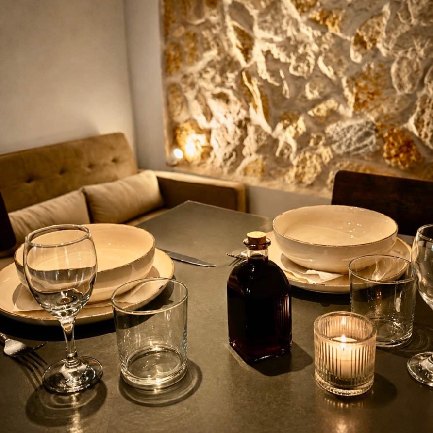 Dining table set for two beside an exposed stone wall