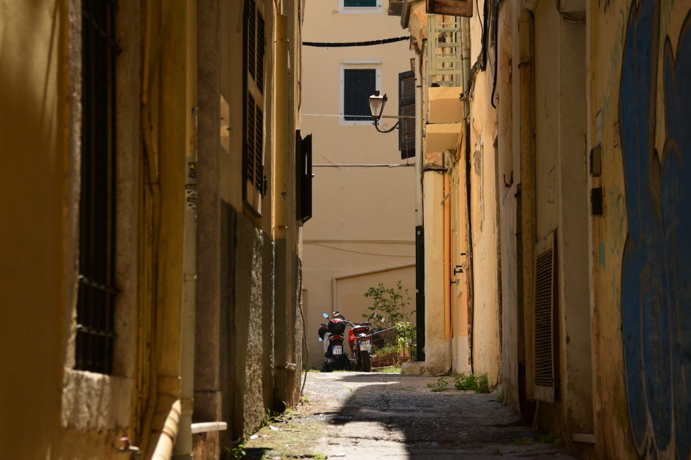 Narrow shaded lane between tall shuttered buildings in Corfu Old Town